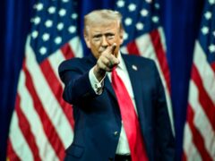 President Donald Trump gestures to the crowd after delivering remarks on stage in front of American flags
